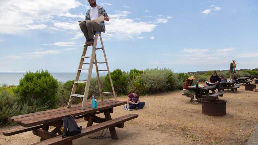 Nikko Mueller sitting on a ladder on top of a park table at the San Clemente Border Station for "Three Border Ecologies" | Lena Martinez Miller
