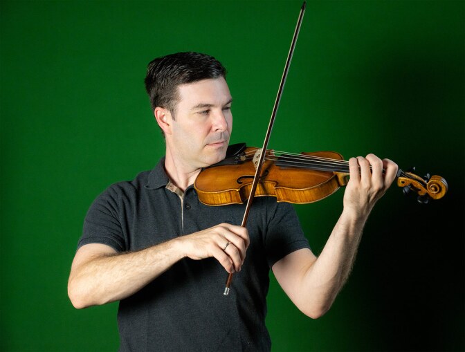 Nathan Cole plays the violin in front of a green wall. | Courtesy of Nathan Cole