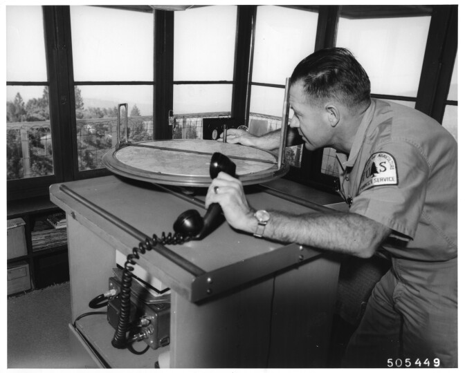 Man stands using circular fire spotting device inside a fire lookout tower