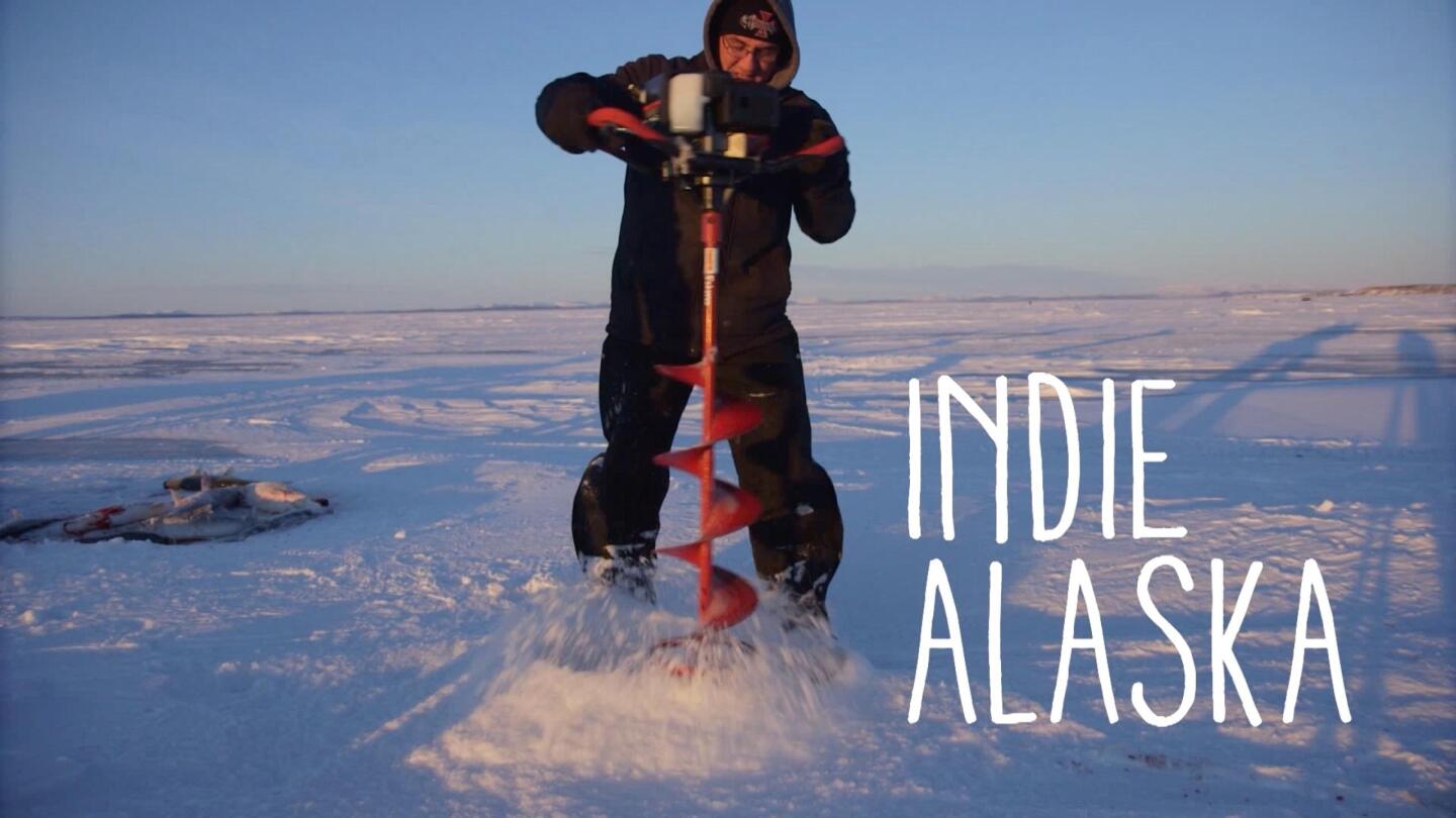 An ice fisherman digs a hole in the ice.