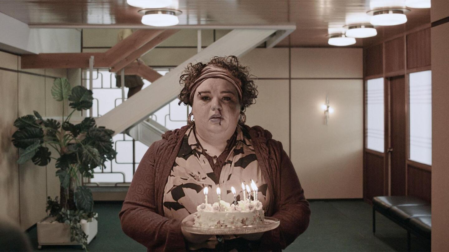 A woman with blood trailing down from her nose holds a cake with lit candles. | From "Professor T: Swansong, Part 1"