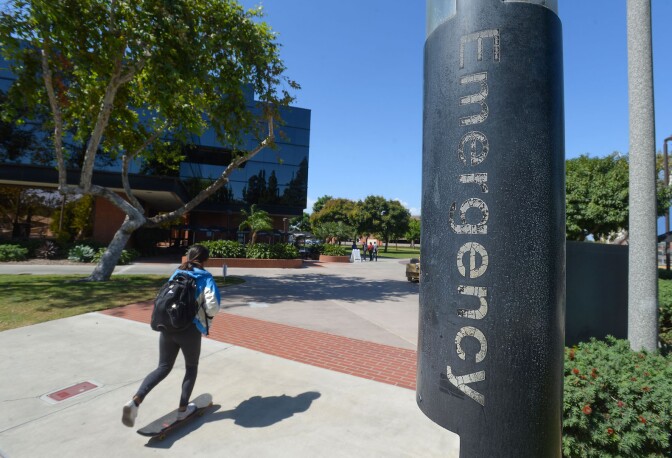 Girl on skateboard, riding past Emergency sign on Cal State Long Beach's campus