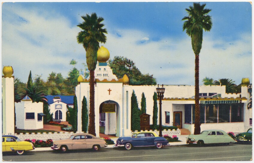 An illustrated postcard of the Self-Realization Fellowship Church of All Religious and India Center. The building sits alone a street lined with parked vintage cars along the curb. The building is white with ornate gold embellishments on posts. There is a small golden cross on the front face of the building over an entrance arch. Two palm trees sit in front of the building.