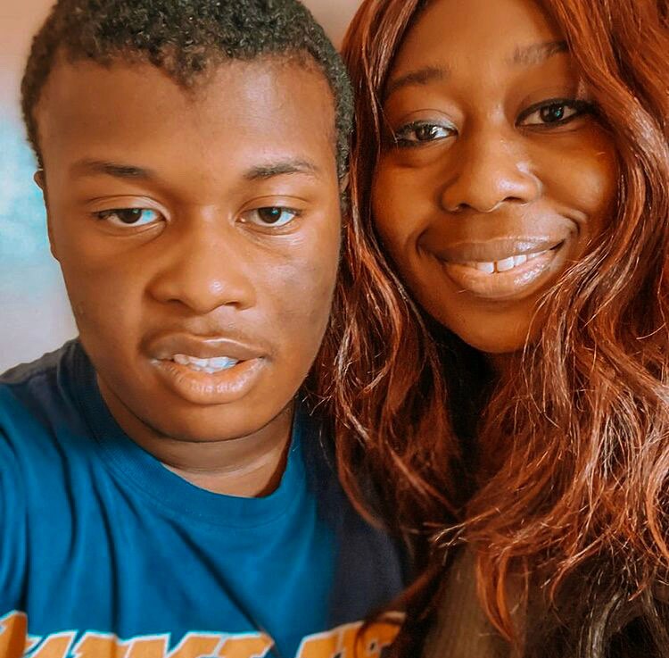 A Black mother with long brown hair smiles next to a Black child.