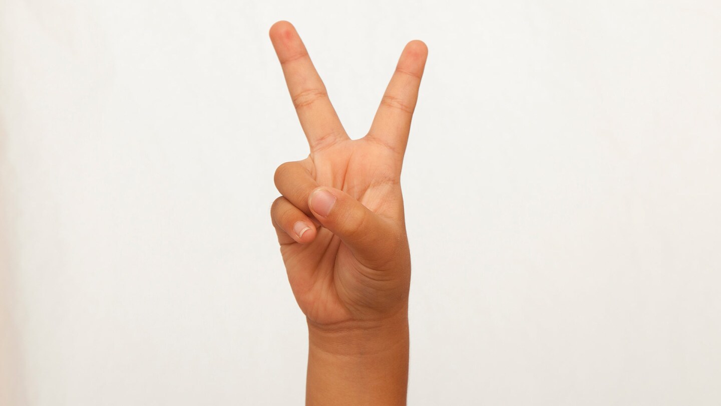 A small child's hand makes a V shape with the fingers.