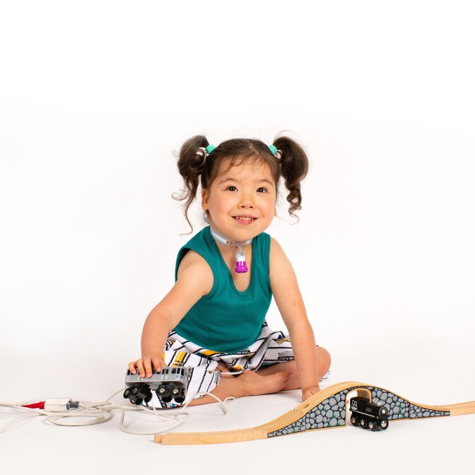 A young girl with a tracheostomy tube playing with trains