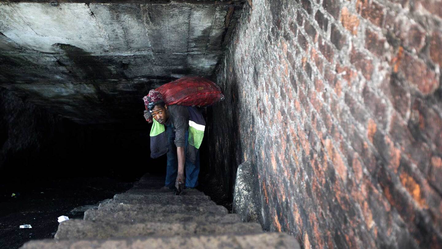 A miner emerges from an abandoned mine in South Africa carrying a heavy sack of coal on his back. | Courtesy of of Thomson Reuters Foundation