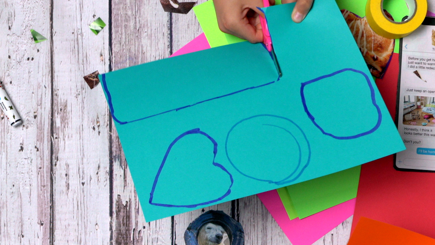 A small child cuts out shapes from colorful construction paper.