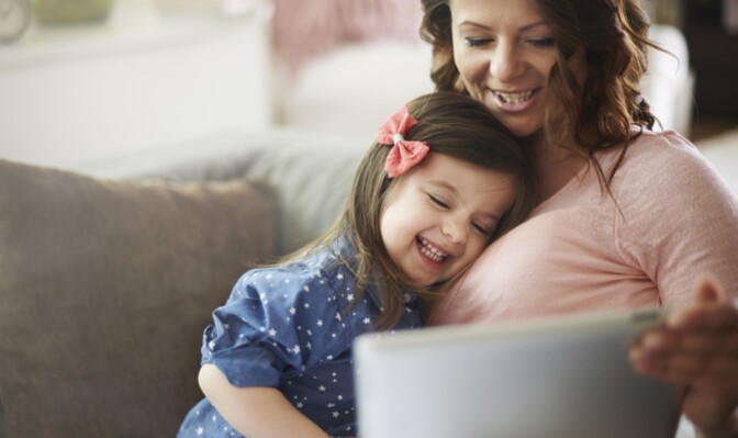 A woman and a little girl sit on a couch in front of a laptop.