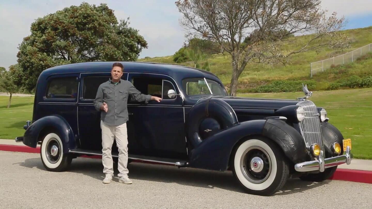Host Mark Walberg stands next to a vintage automobile.