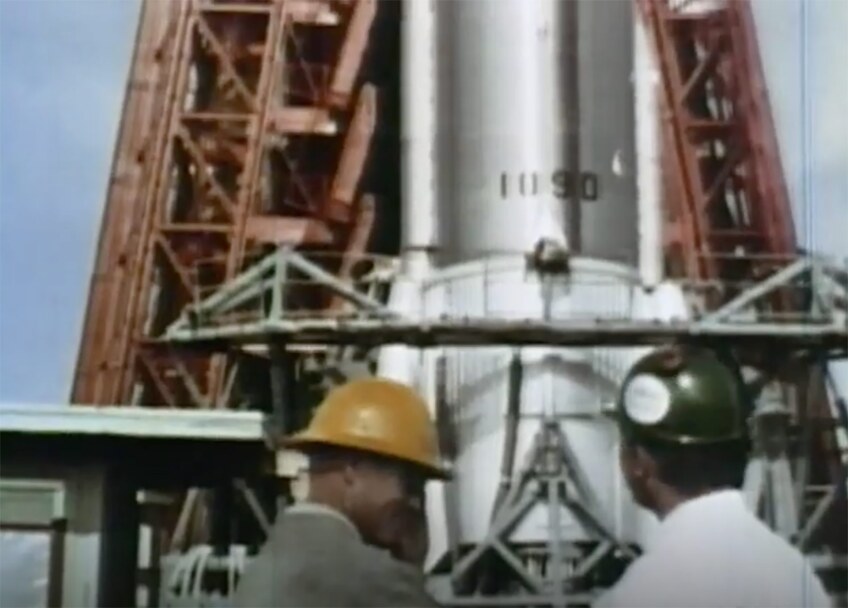 Two men stand at the base of a rocket