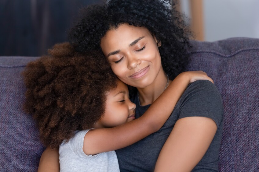 Closeup Black daughter embracing mother sitting on couch at home
