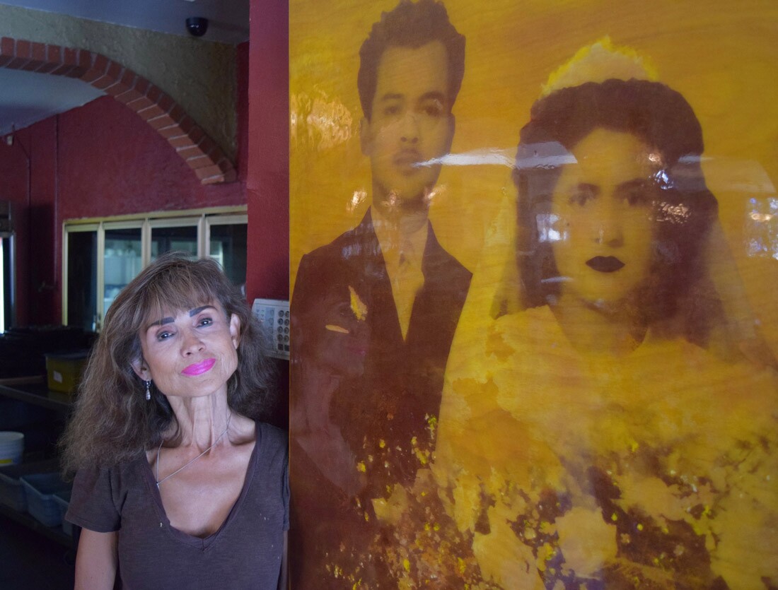 Angie Montes beside a portrait of her parents, Irene and Gustavo, on their wedding day. The image was printed on birch wood by artist Chassidy Rana.
