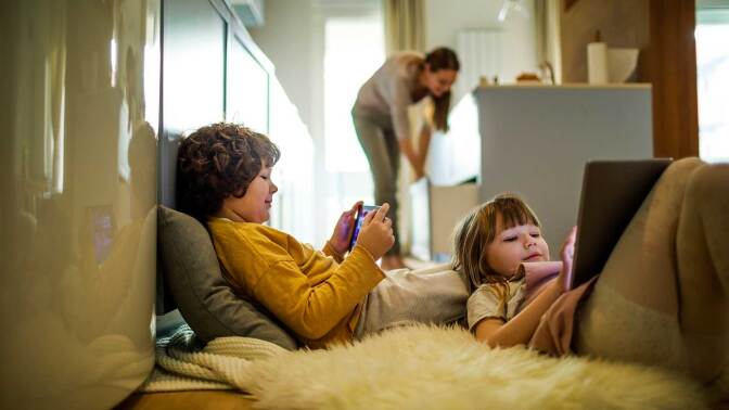 two children relax on the floor while watching their devices