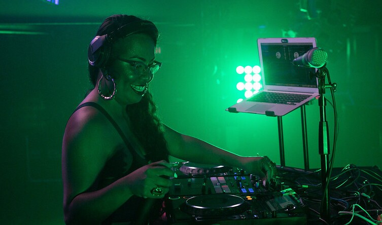 DJ Sizzle Fantastic performs in a room lit in green light.
