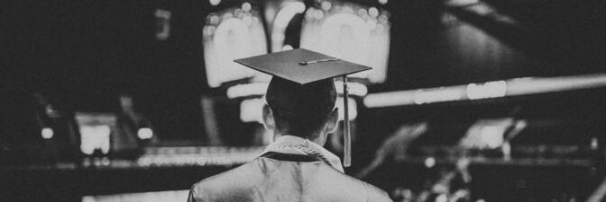 Black and white photograph of a student in a cap and gown facing an auditorium.