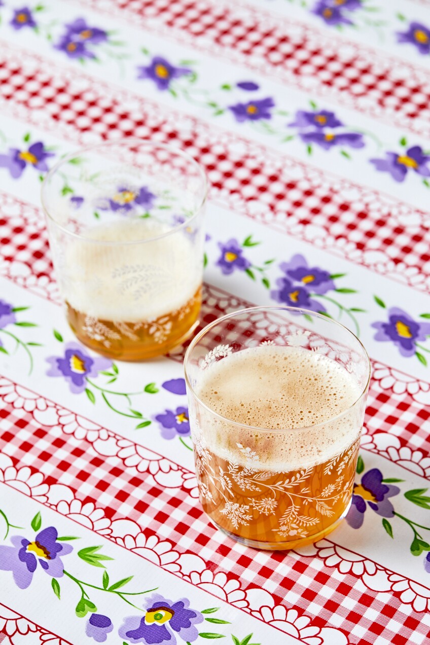 A fizzy Russian drink called Kvass pictured in two glasses with a checkered and floral table cloth.