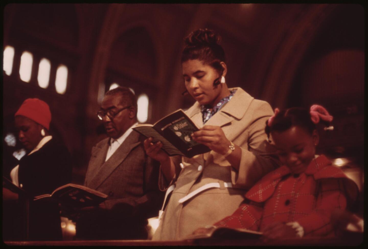 A group of people stand while reading a bible in church.