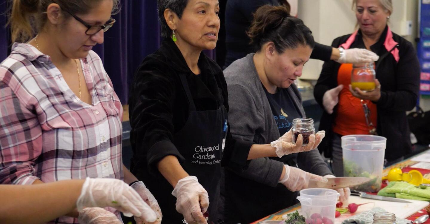 Women stand beside each other as they prepare food to serve.