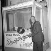 An African American man holds a record while leaning on a music booth.