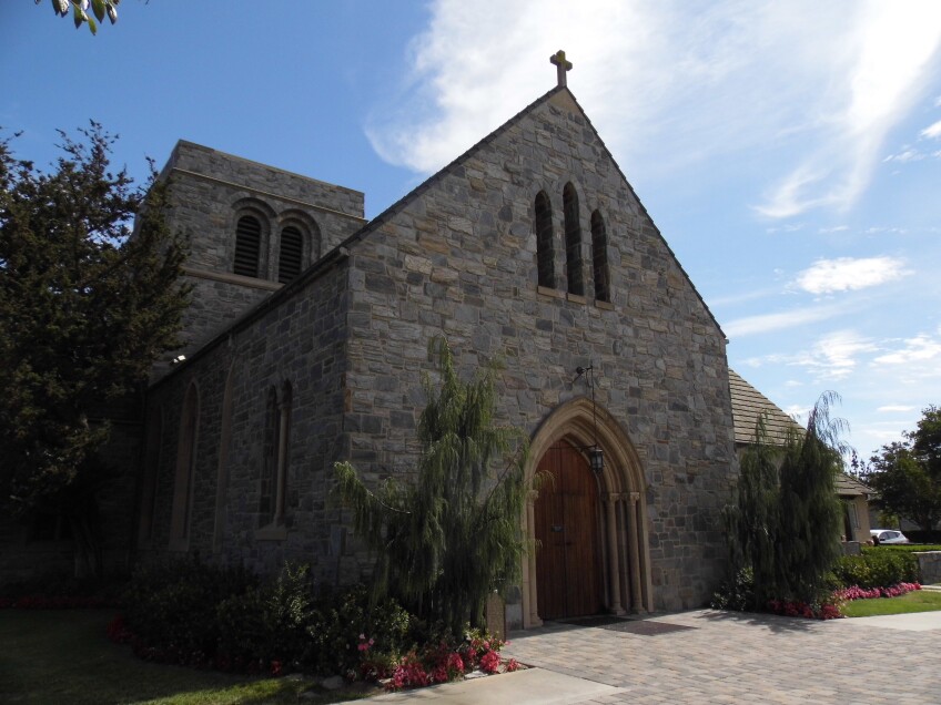 A church with gray and beige cobblestoned exterior walls and a small cross atop the tip of the roof. 