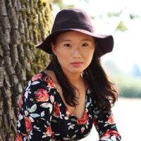 A profile photo of KCET writer Olivia Wolf. She is wearing a black floppy hat and a dress with roses on it. Behind her is a nature landscape.