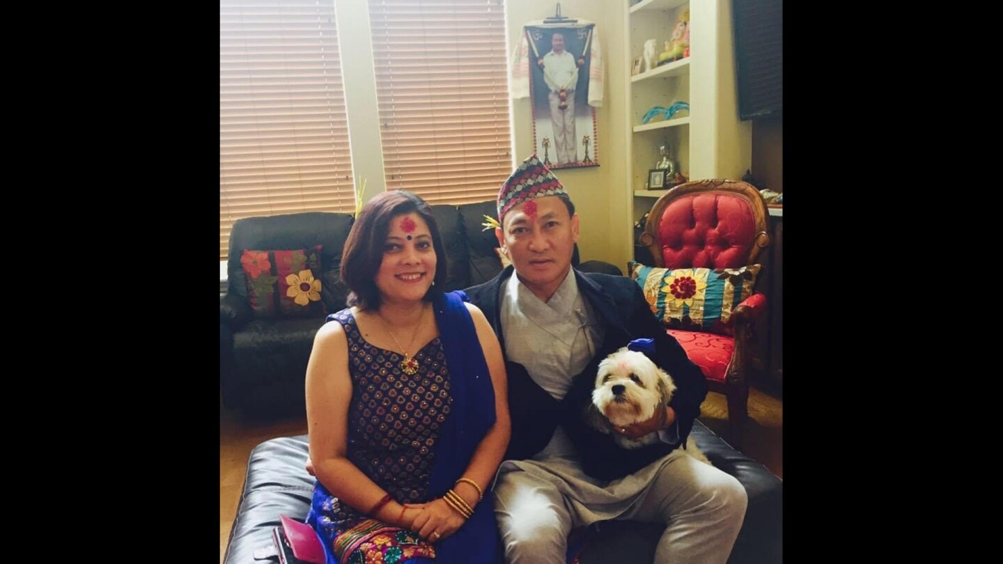 A woman and man in festive clothes sit together holding a small white dog.