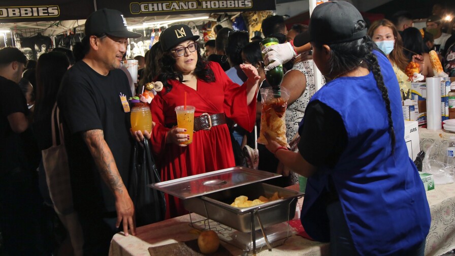 An Asian American man with a baseball cap and a woman in red and a cap order food from a food stall at Avenue 26 night market in Lincoln Heights.
