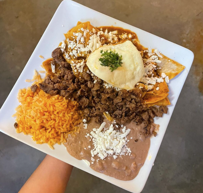 A plate of chilaquiles is photographed from above. It's served with rice and refried beans on the side.