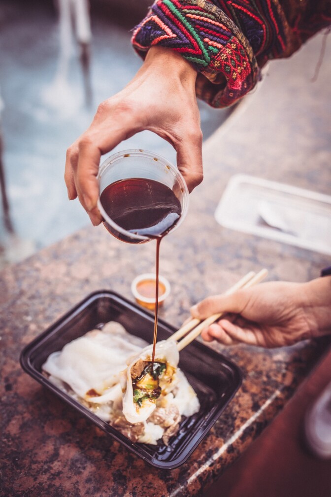 A man pouring sauce over marinated beef & shrimp with chives rice noodle roll from Yin Ji Chang Fen