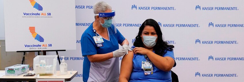 Governor Gavin Newsom looks on, far right, as ICU nurse Helen Cordova receives the Pfizer-BioNTech COVID-19 vaccine at Kaiser Permanente Los Angeles Medical Center in Los Angeles, California on December 14, 2020. | JAE HONG/POOL/AFP via Getty Images