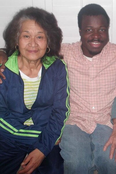 A young person smiles as they wrap their arm around an older person. 