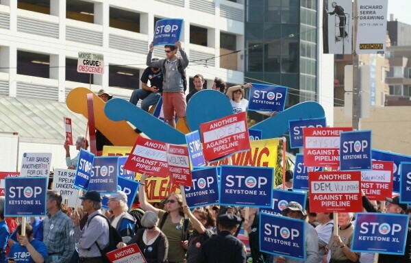 Protestors against the construction of the Keystone XL oil pipeline hold signs and stand on a Keith Haring sculpture as they demonstrate in San Francisco before the arrival of U.S. President Barack Obama | Photo by Justin Sullivan/Getty Images