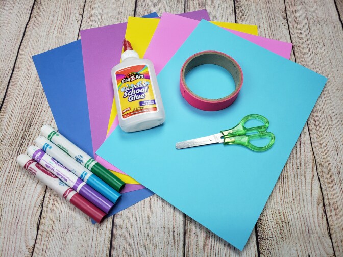 construction paper, markers, glue, tape and scissors are laid out on a wooden table