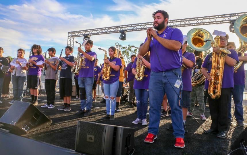 A youth band with wind instruments stand on stage.