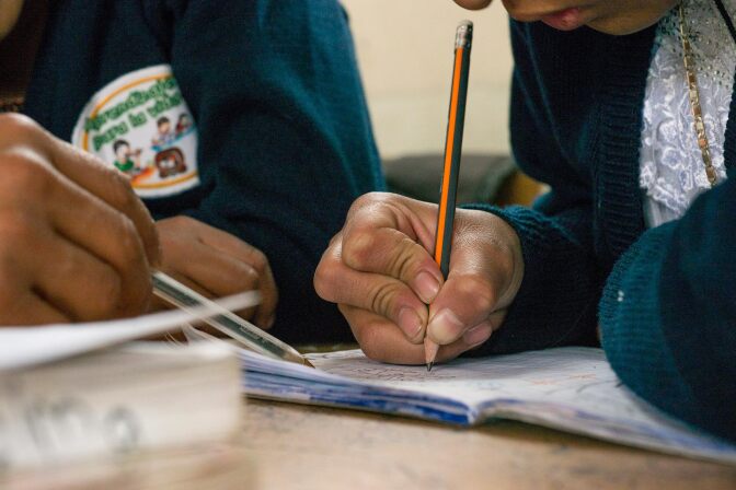 A girl writes on a notebook as her teacher guides her.