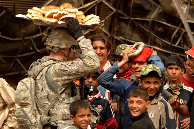 A group of Iraqi children look on as a U.S. Soldier practices balancing a plate of bread on his head in the Jameela market area of the Sadr City district of Baghdad, Iraq. | Tech. Sgt. Cohen A. Young / United States Forces Iraq/ Flickr