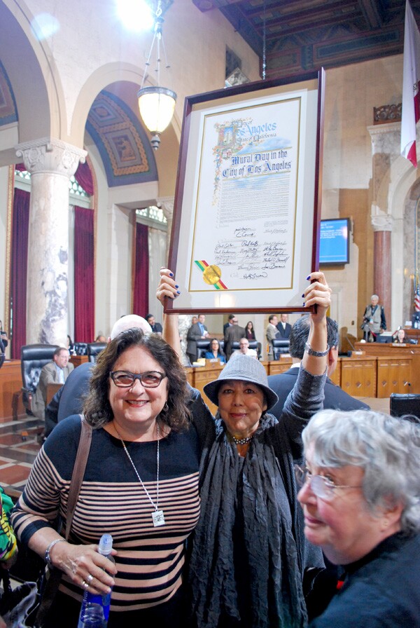 Rojas-Williams (center) holds up the proclamation of ''Mural Day in the City of Los Angeles. Muralists Judy Baca (left) and Emily Winters (right) look on I Photo: MCLA