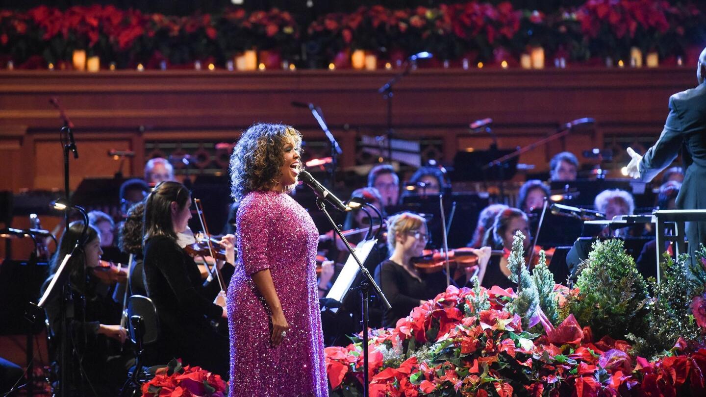 A singer performs on stage with an orchestra beside her.