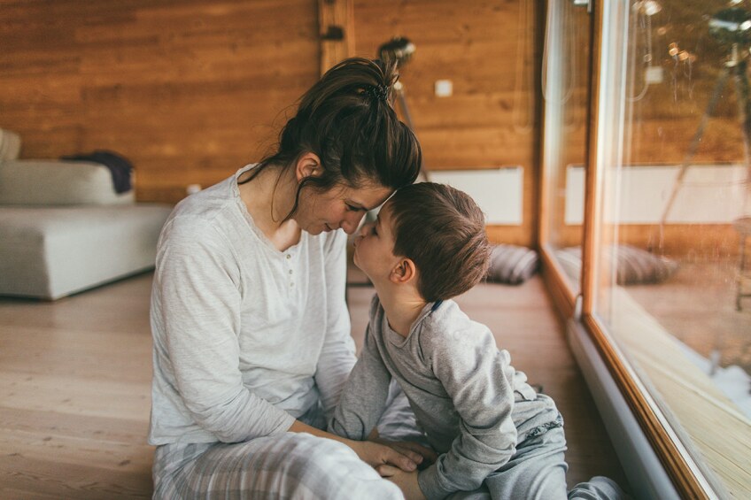 A parent and child wearing pajamas hold their heads close to each other. istock
