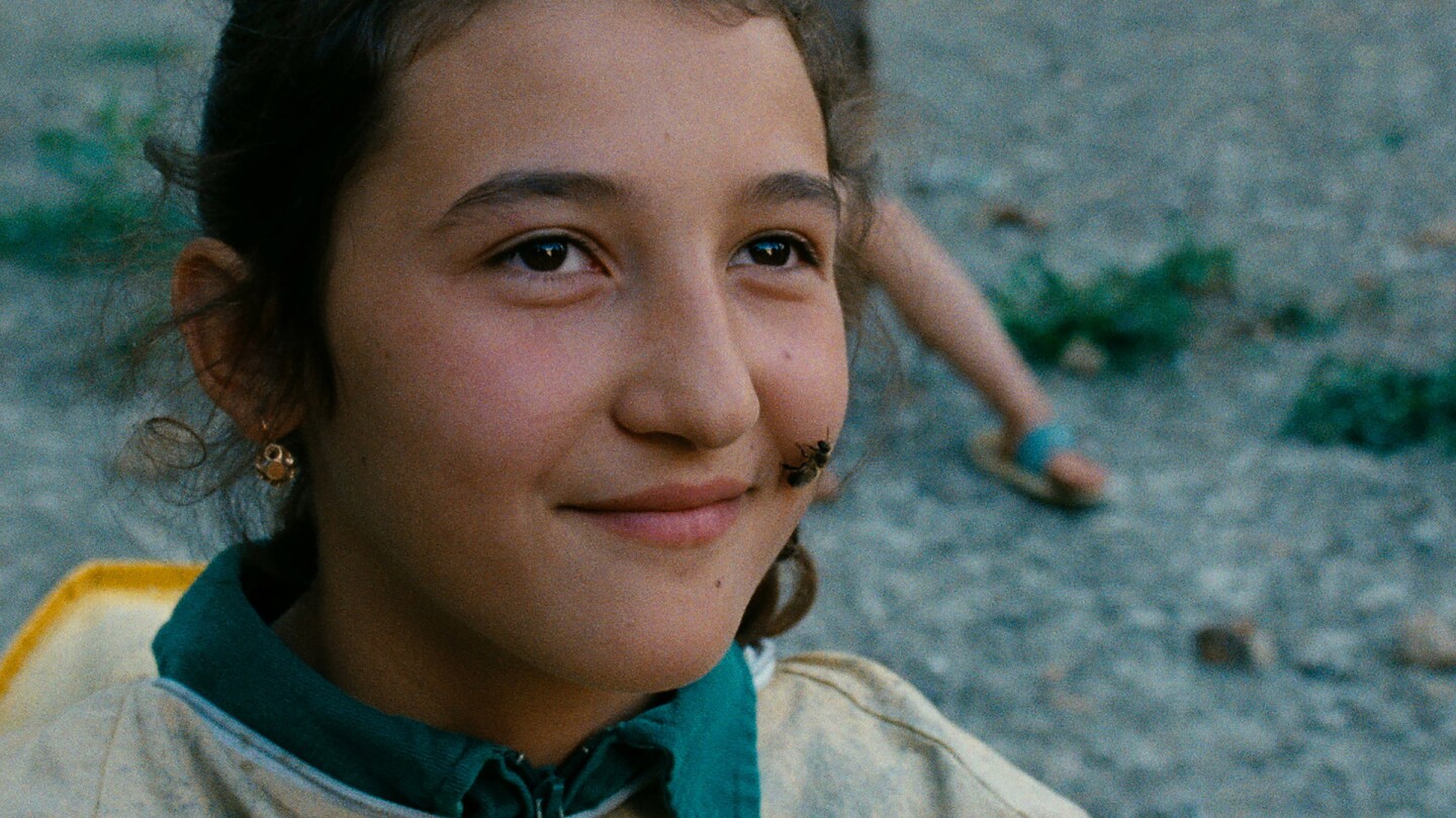 A young person smiles with a bee on her face.
