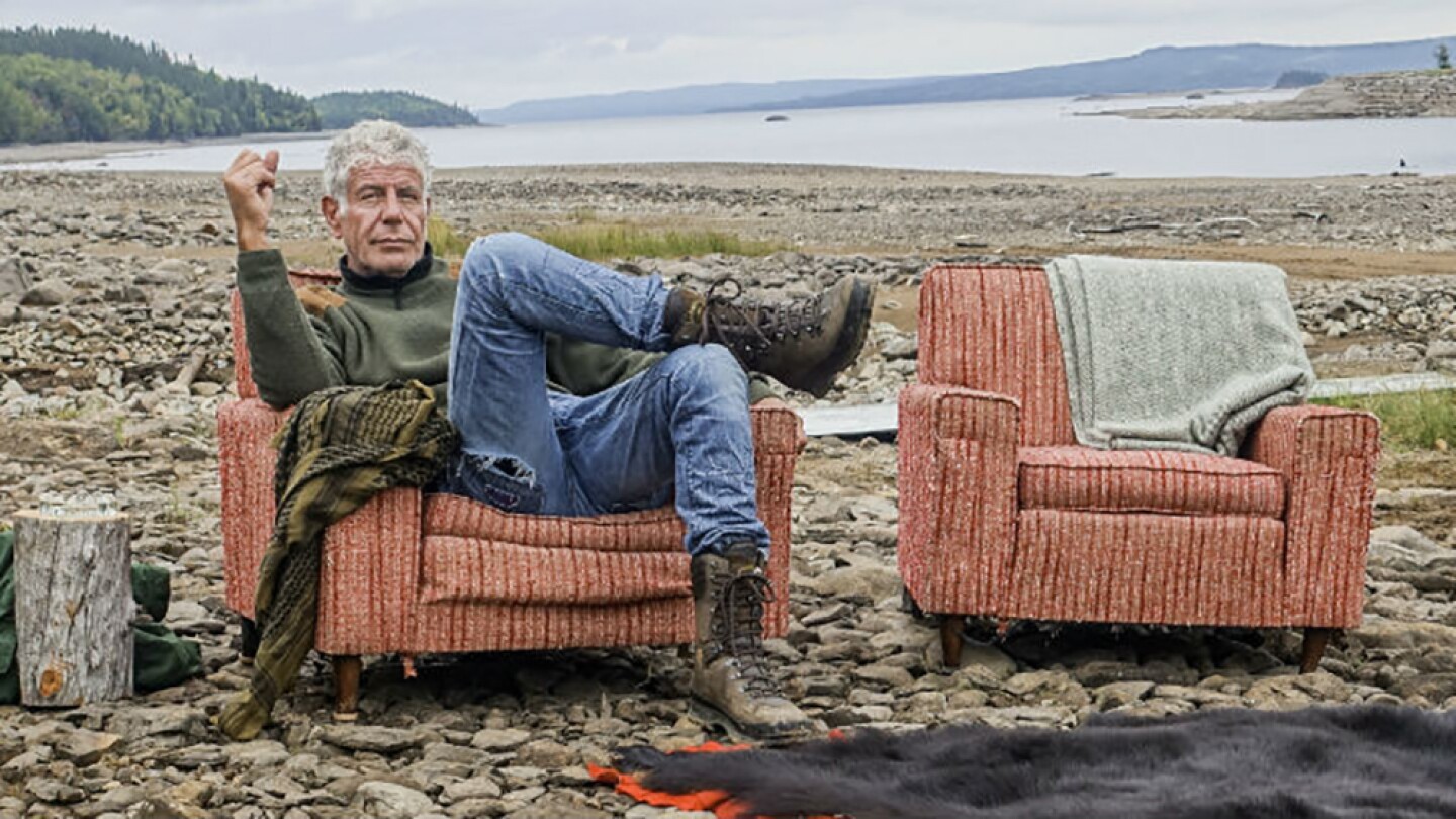 Anthony Bourdain poses in an armchair placed near a lake.