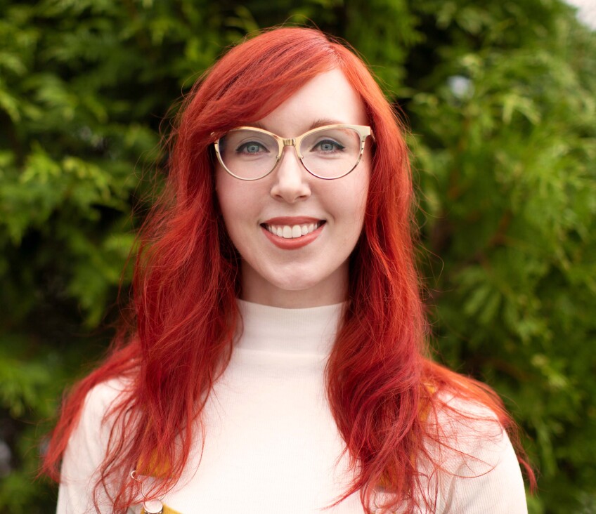 A red-haired woman with long hair smiling at the camera.