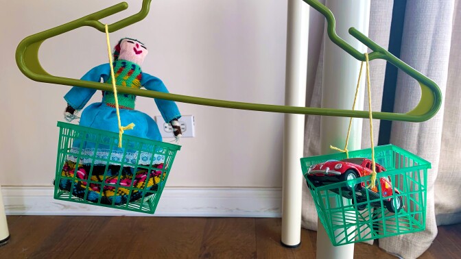 a Tarahumara doll and a small toy car hang in a balance scale made out of a hanger and berry containers