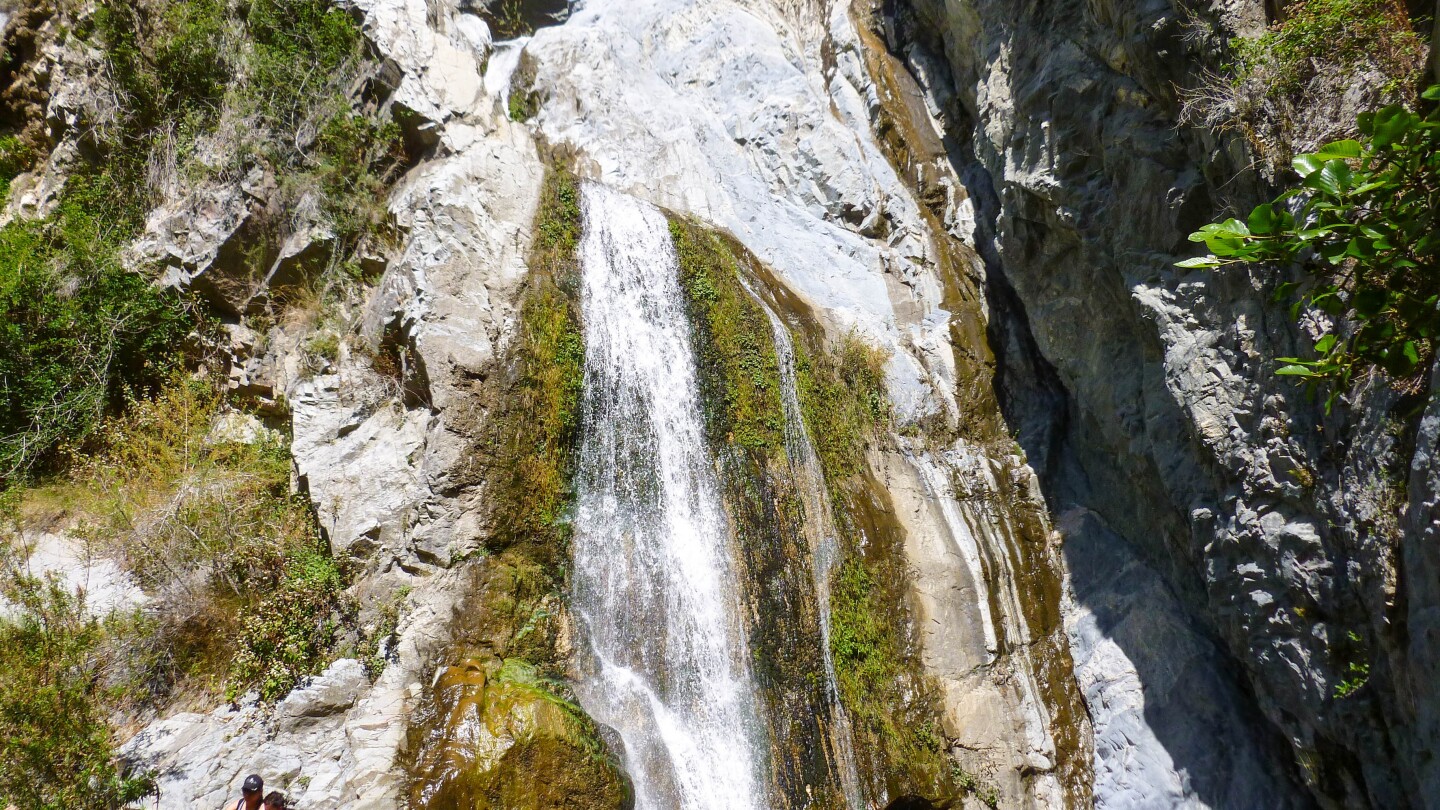 The waterfall at Fish Creek in the Angeles National Forest. To the bottom left corner are two hikers resting by the creek.