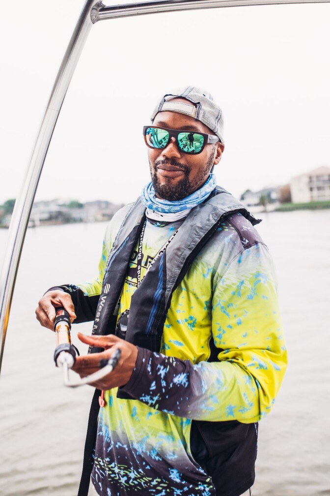 A man stands on a fishing boat. Behind him is a view of Clear Lake, Texas.