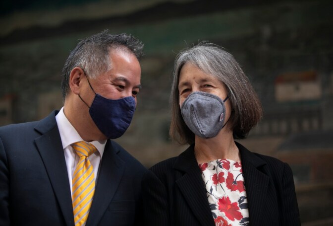 Two lawmakers wearing suits and masks talking to each other