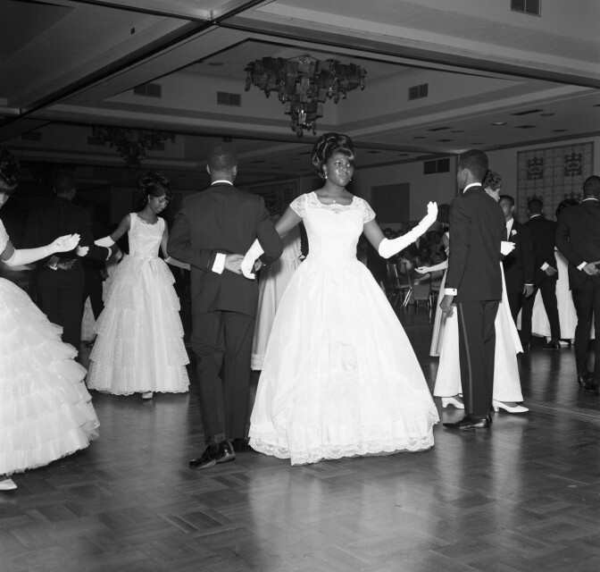 African American debutantes dance with their escorts on the dance floor.