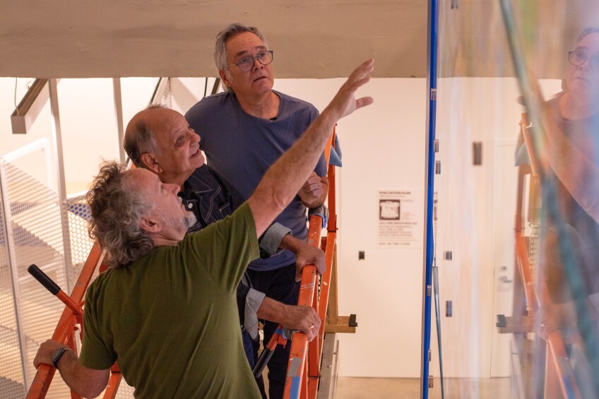 Three men look at a large piece of artwork
