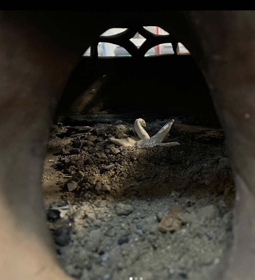 Leftover shards of ceramic are arranged in a pile of ashes to look like a swan. The swan sits inside a small clay dome.
